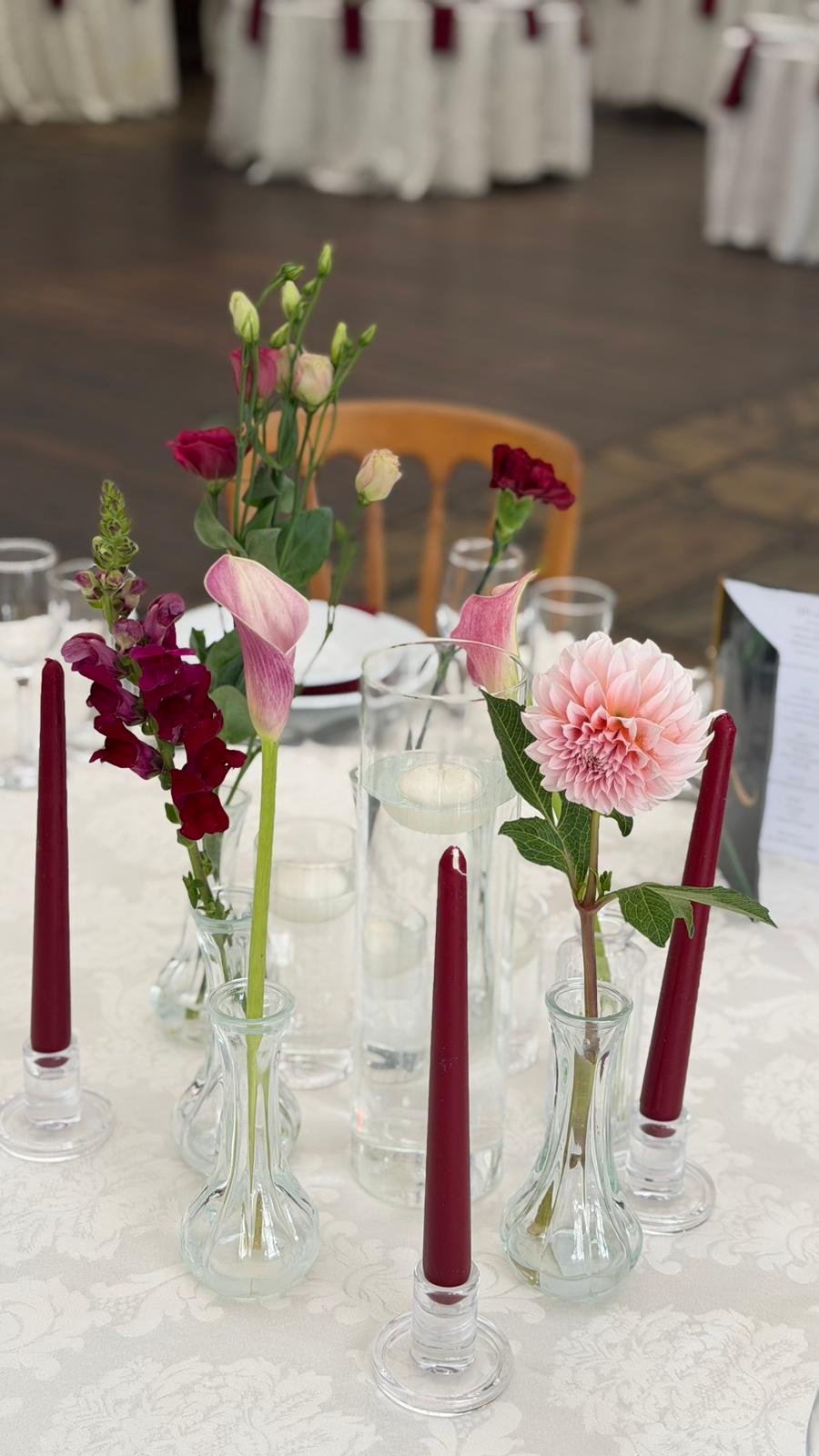 Burgundy taper candles and single stems in small glass vases on an ivory tablecloth